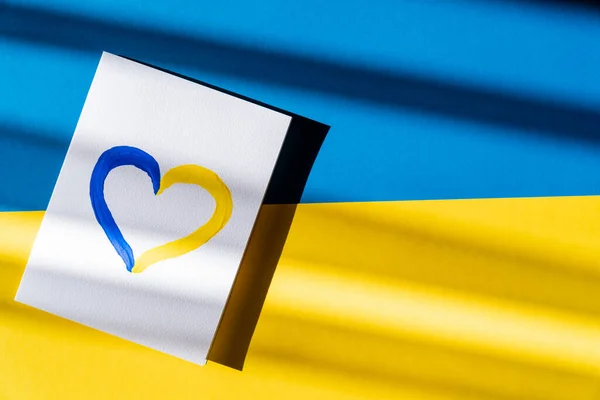 Vue du dessus du panneau de coeur jaune et bleu peint sur la carte sur le drapeau ukrainien — Photo de stock