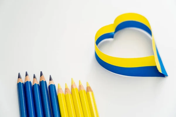 Vue du dessus des crayons bleus et jaunes près du ruban en signe de coeur sur fond blanc — Photo de stock