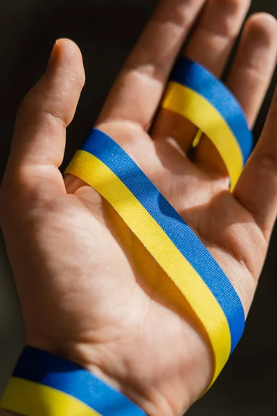 Cropped view of blue and yellow ribbon on blurred male hand on black background — Stock Photo