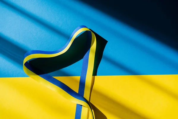 Top view of ribbon in heart shape with shadow on ukrainian flag — Stock Photo