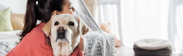 Preteen girl embracing labrador dog at home, banner — Stock Photo