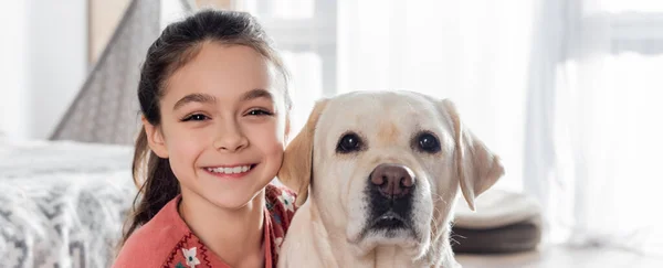 Feliz chica morena sonriendo a la cámara cerca divertido perro labrador, pancarta - foto de stock