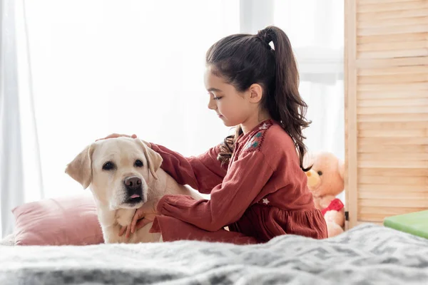 Seitenansicht brünettes Mädchen mit Pferdeschwanz streichelt Labrador auf verschwommenem Vordergrund — Stockfoto