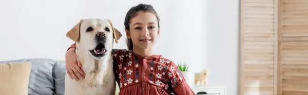 Positive girl hugging labrador dog and looking at camera, banner — Stock Photo