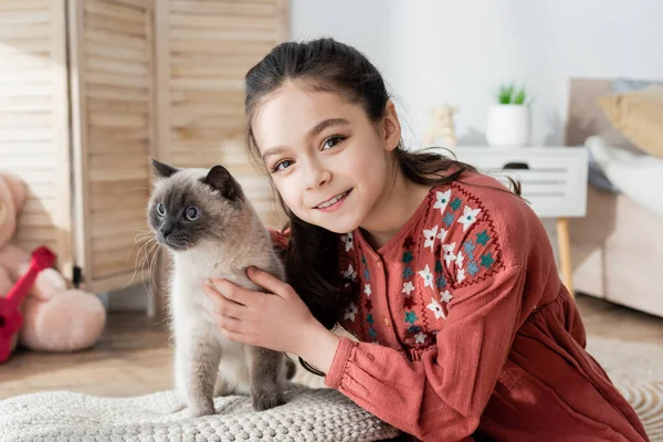 Alegre preadolescente chica abrazando mullido gato y mirando a la cámara - foto de stock