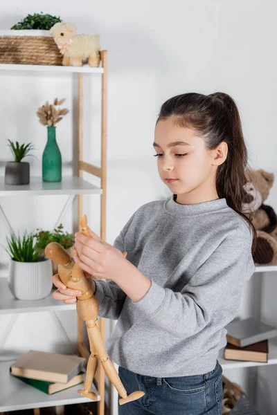 Preteen girl holding toy human figurine near blurred rack with flowerpots — Stock Photo