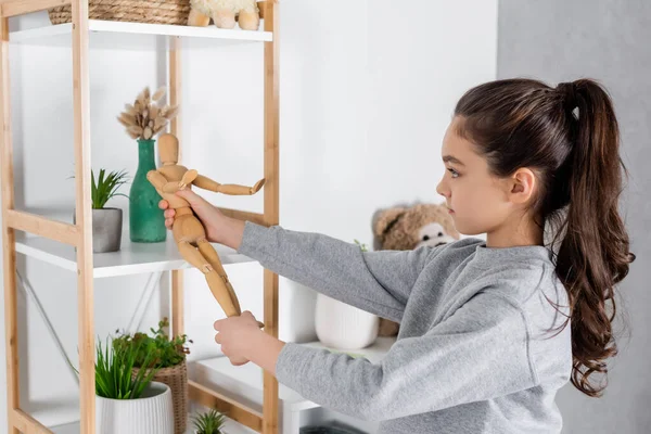 Side view of girl playing with toy human figurine near rack with potted plants — Stock Photo