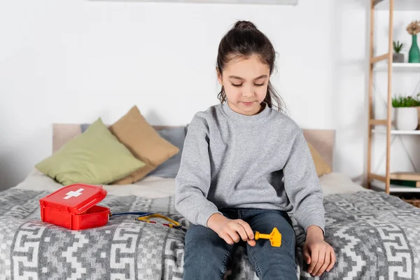 Fille examen genou avec jouet neurologique malleus près de la trousse de premiers soins sur le lit — Photo de stock