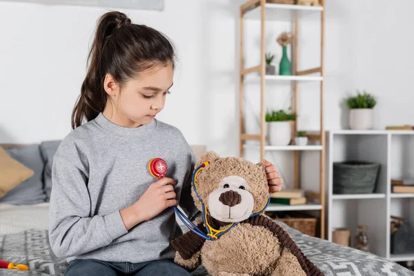 Mädchen spielt Arzt mit Teddybär und Spielzeug-Stethoskop im Schlafzimmer — Stockfoto