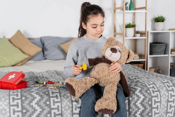 Preteen girl examining teddy bear with toy neurological malleus in bedroom — Stock Photo