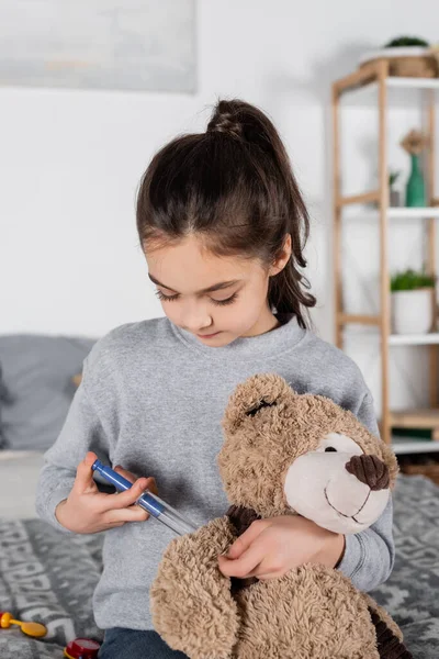 Brunette preteen girl making injection to teddy bear with toy syringe — Stock Photo