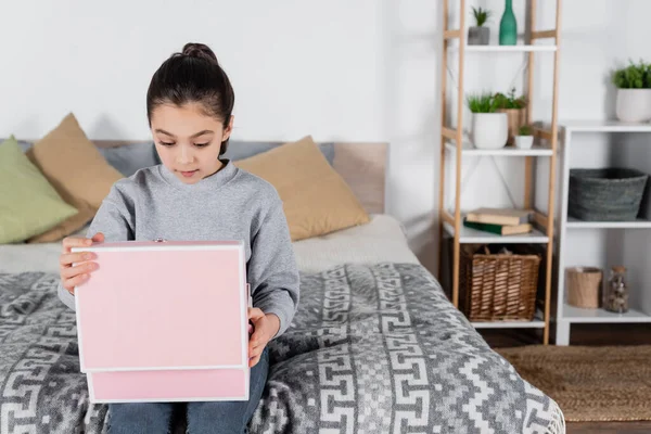 Amazed girl sitting on bed and looking into pink gift box — Stock Photo