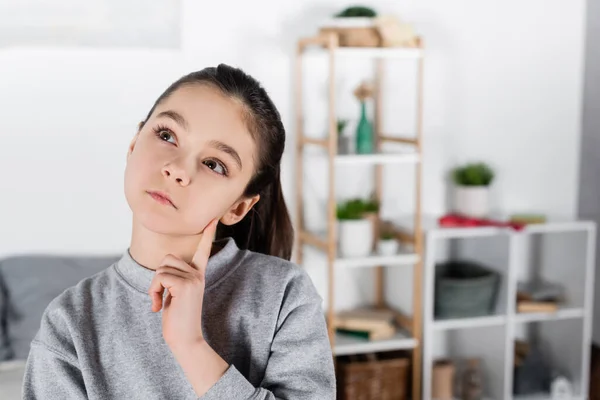 Nachdenkliches Mädchen, das Gesicht berührt und auf verschwommenem Hintergrund wegsieht — Stockfoto