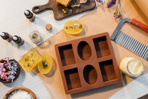 Vista superior de sabão artesanal perto de molde de silicone, flores e óleos essenciais na mesa — Fotografia de Stock
