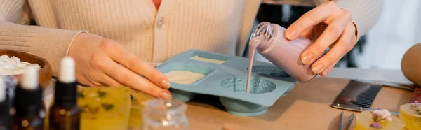 Cropped view of craftswoman pouring liquid soap in silicone mold near blurred essential oils, banner — Stock Photo