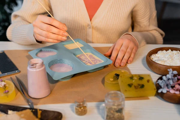 Ausgeschnittene Ansicht der Handwerkerin, die Muster auf Seife in Silikonform in der Nähe von Vorräten auf dem Tisch herstellt — Stockfoto