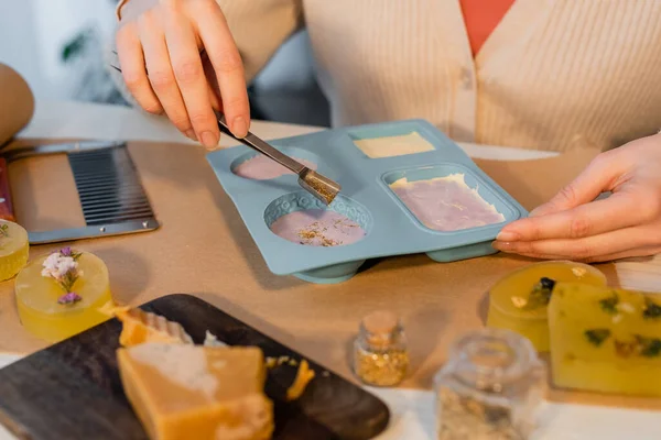 Ausgeschnittene Ansicht einer Handwerkerin, die Safran auf Seife in Silikonform auf Bastelpapier auf dem Tisch gießt — Stockfoto