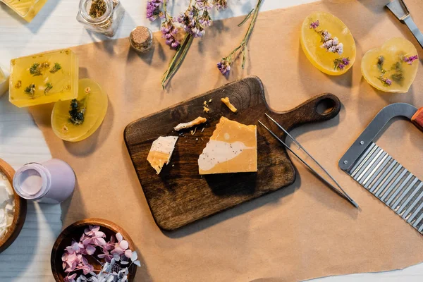 Vue du dessus du savon artisanal sur planche à découper près des fleurs sèches et des fournitures sur papier — Photo de stock