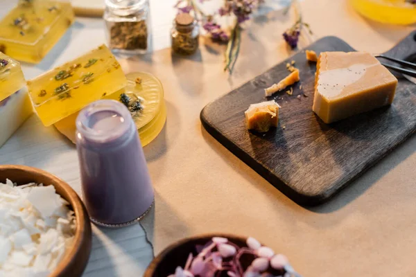 Savon fait main sur planche à découper en bois près de fleurs sèches sur fond flou — Photo de stock