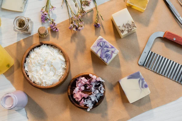 Vue du dessus des flocons de savon près des fleurs et des barres sur du papier artisanal sur la table — Photo de stock