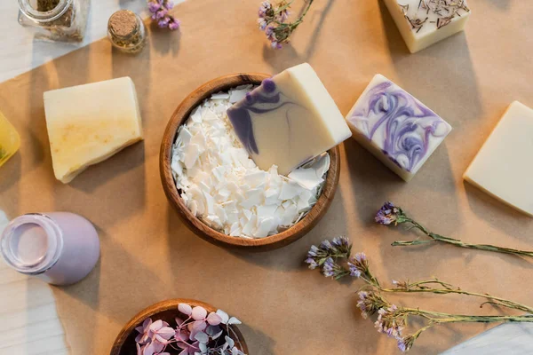 Vista dall'alto del sapone fatto a mano in ciotola con fiocchi vicino a fiori su carta artigianale — Foto stock