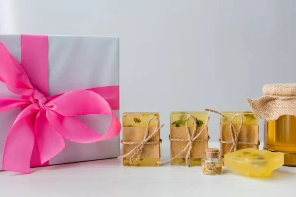 Geschenk-Box in der Nähe von handgemachten Seifenstangen und Glas mit Honig auf grauem Hintergrund — Stockfoto