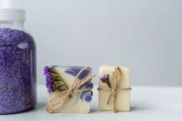 Vue rapprochée du sel de mer près du savon artisanal avec des fleurs sur fond gris — Photo de stock