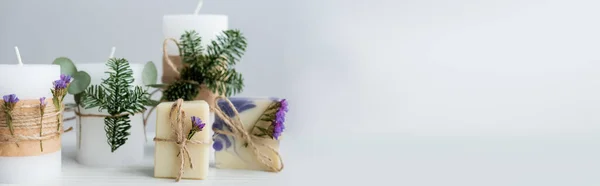 Handgemachte Seife mit Blumen neben Kerzen mit Tannenzweigen auf grauem Hintergrund, Banner — Stockfoto