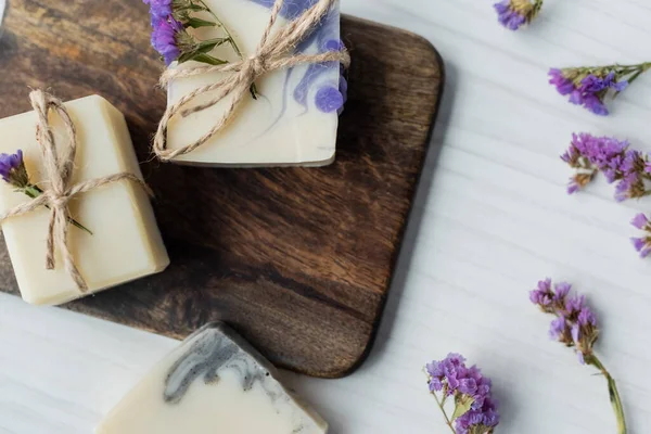 Vue du dessus des barres de savon faites à la main sur la planche à découper près des fleurs sèches sur la table — Photo de stock