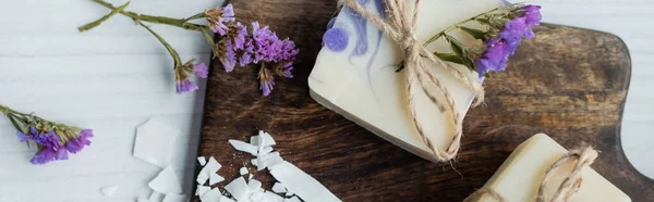 Vue du dessus du savon artisanal avec des fleurs sur la planche à découper sur la table, bannière — Photo de stock