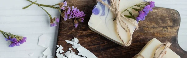 Vue du dessus du savon artisanal avec des fleurs sur la planche à découper sur la table, bannière — Photo de stock