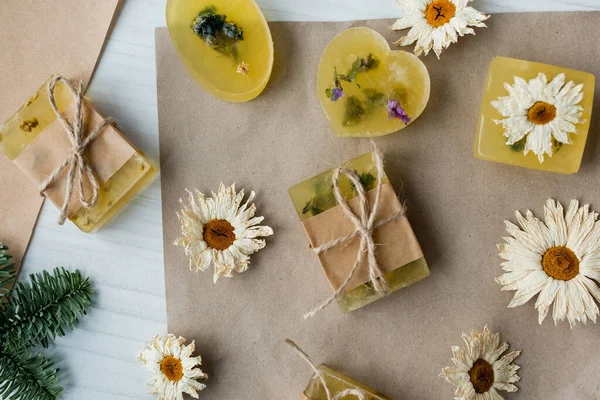 Vue du dessus du savon fait à la main près des camomilles sèches sur du papier artisanal sur table — Photo de stock