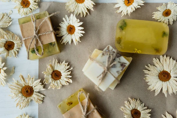 Vue du dessus des barres de savon faites à la main près des fleurs sèches sur du papier artisanal — Photo de stock