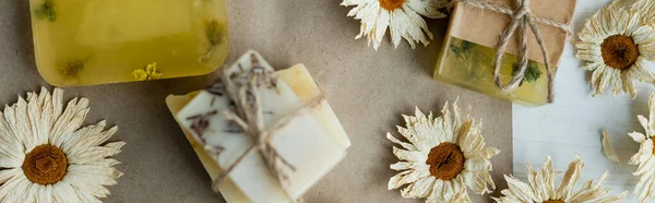 Vista dall'alto di fiori di camomilla secchi vicino alle saponette su carta artigianale, banner — Foto stock