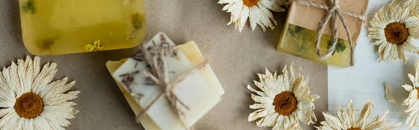 Top view of dry chamomile flowers near soap bars on craft paper, banner — Stock Photo