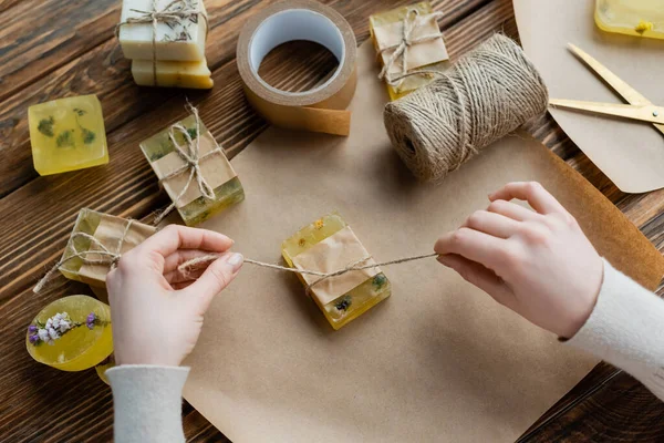 Top view of craftswoman holding twine near craft soap on paper at home — Stock Photo