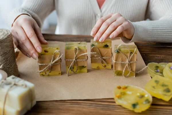 Cropped view of craftswoman touching handmade soap bars near twine and craft paper at home — Stock Photo
