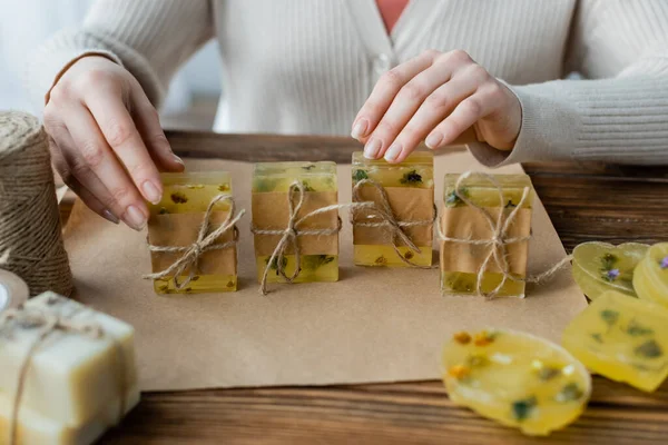 Vue recadrée de l'artisan touchant des barres de savon faites à la main près de ficelle et de papier artisanal à la maison — Photo de stock