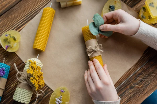 Vista superior da artesã decorando vela artesanal com eucalipto perto de barras de sabão em casa — Fotografia de Stock