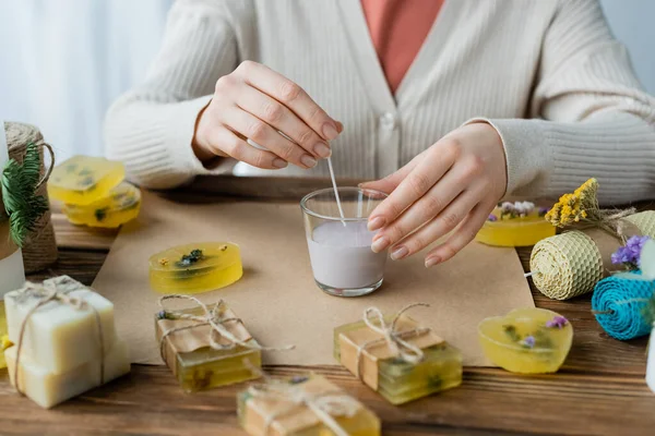 Cropped view of craftswoman holding wick while making candle in glass near soap on table — Stock Photo