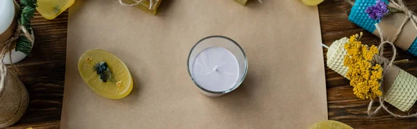 Top view of candle in glass near soap on craft paper on wooden surface, banner — Stock Photo