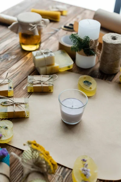 Bougie faite à la main en verre près des barres de savon et du papier artisanal sur une surface en bois — Photo de stock