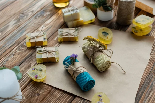 Vista ad alto angolo di candele fatte a mano con fiori su carta artigianale vicino sapone su superficie di legno — Foto stock