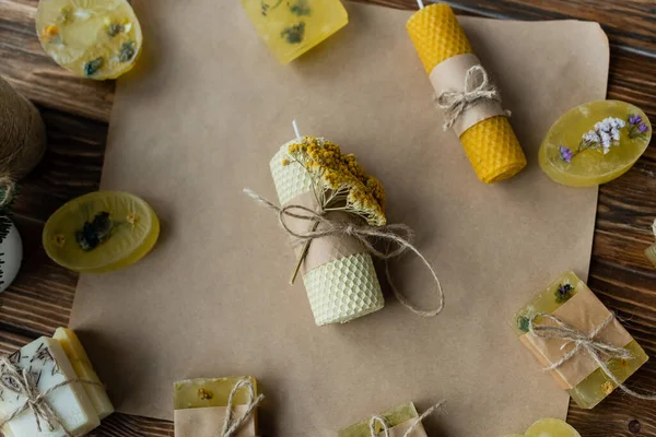 Vue du dessus de la bougie faite à la main avec des fleurs près du savon sur papier artisanal sur surface en bois — Photo de stock