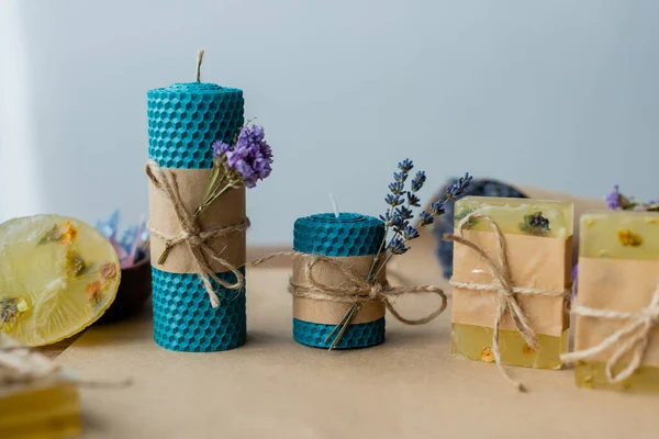 Velas hechas a mano y barras de jabón con flores secas sobre fondo gris - foto de stock