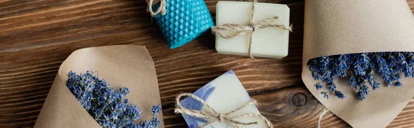 Top view of bouquets of lavender near craft soap and candle on wooden surface, banner — Stock Photo