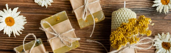 Top view of homemade soap bars, candle and dry chamomiles on wooden surface, banner — Stock Photo
