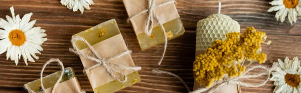 Vue de dessus des barres de savon maison, bougie et camomilles sèches sur la surface en bois, bannière — Photo de stock