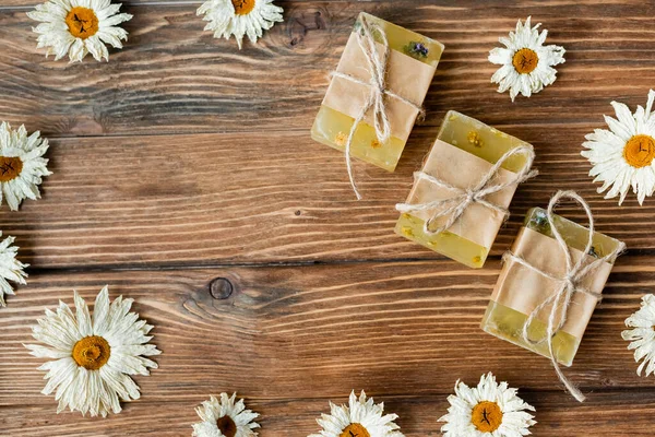 Top view of handmade soap bars in frame from dry romomiles on wooden surface — стоковое фото