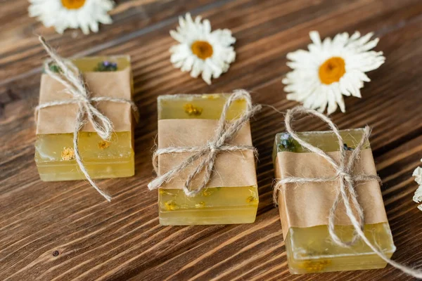 Vue rapprochée des bardes de savon faites à la main près des fleurs floues de camomille sèche sur la surface en bois — Photo de stock